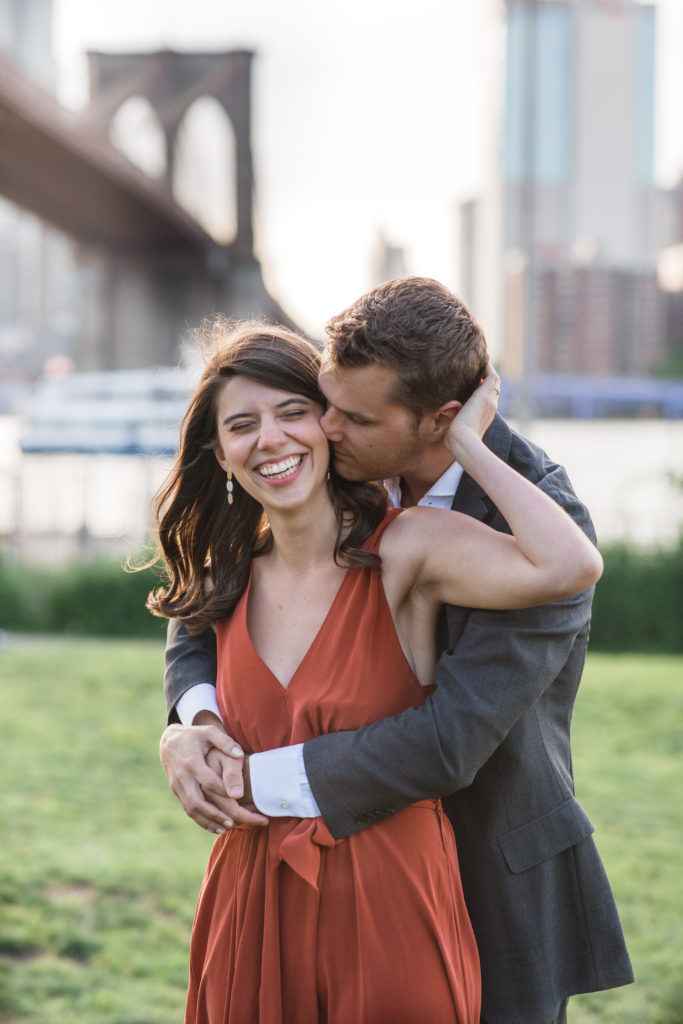 Location of engagement session matters.Beautiful couple softly kissing in Brooklyn Bridge Park with New York City in the background