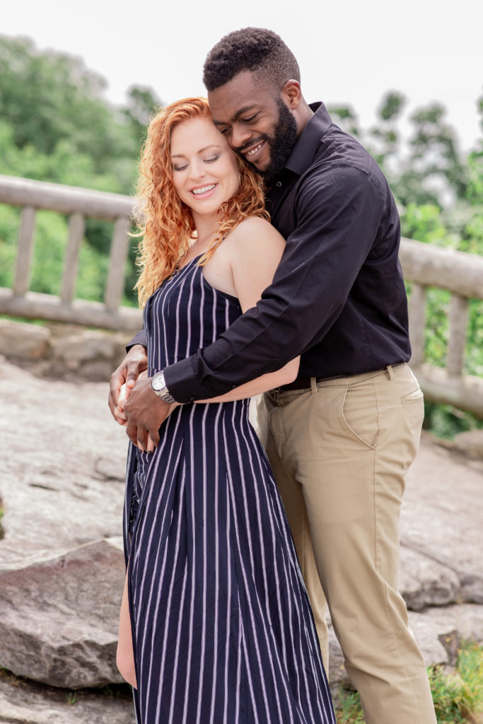 Location of engagement session matters.Interracial couple standing on the overlook at Coopers Rock state forest with beautiful view of West Virginia Mountains behind them
